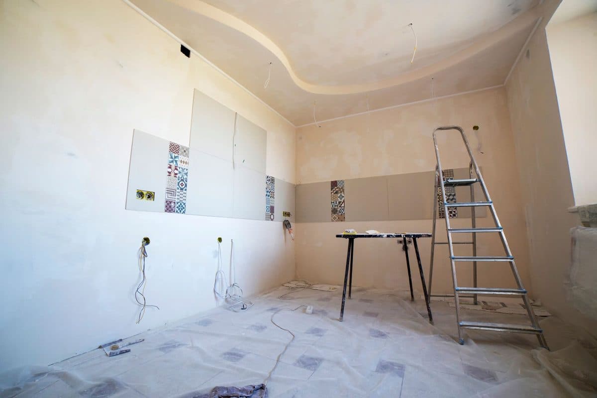 Raum im Umbau mit halb gefliester Wand, offenen Elektrodosen und Trittleiter
